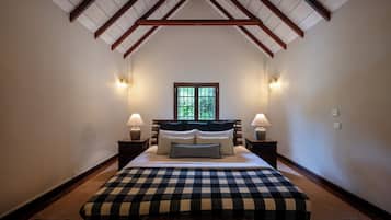 Une chambre avec un plafond haut, un grand lit recouvert d’une courtepointe à carreaux, deux lampes de chevet et une fenêtre donnant sur un paysage verdoyant.