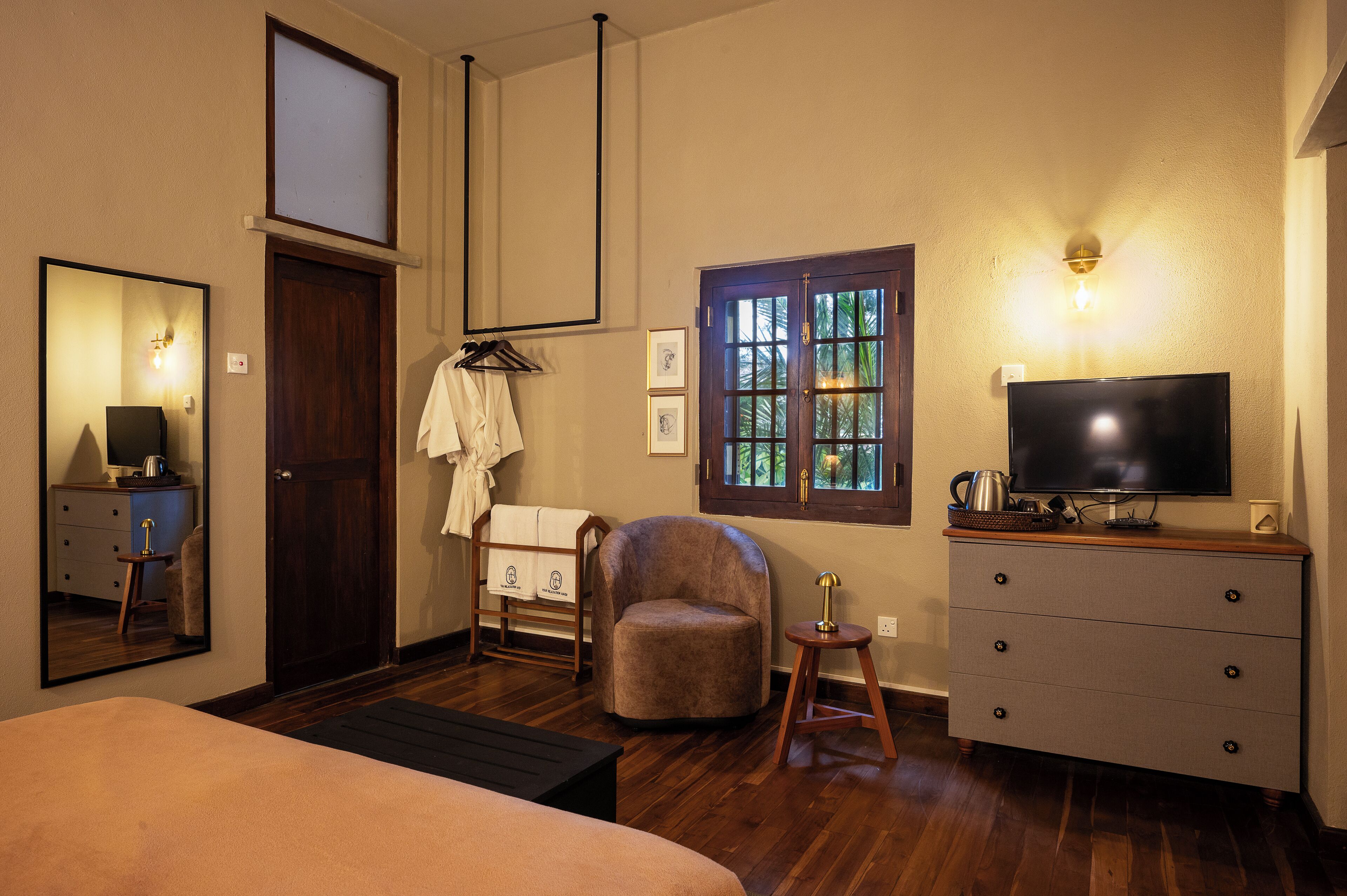 Une chambre d’hôtel avec un lit, une télévision, une commode en bois, une chaise, une fenêtre donnant sur un paysage agréable et un miroir.
