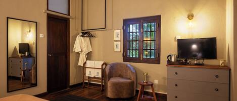 A hotel room with a bed, a TV, a wooden dresser, a chair, a window with a view, and a mirror.