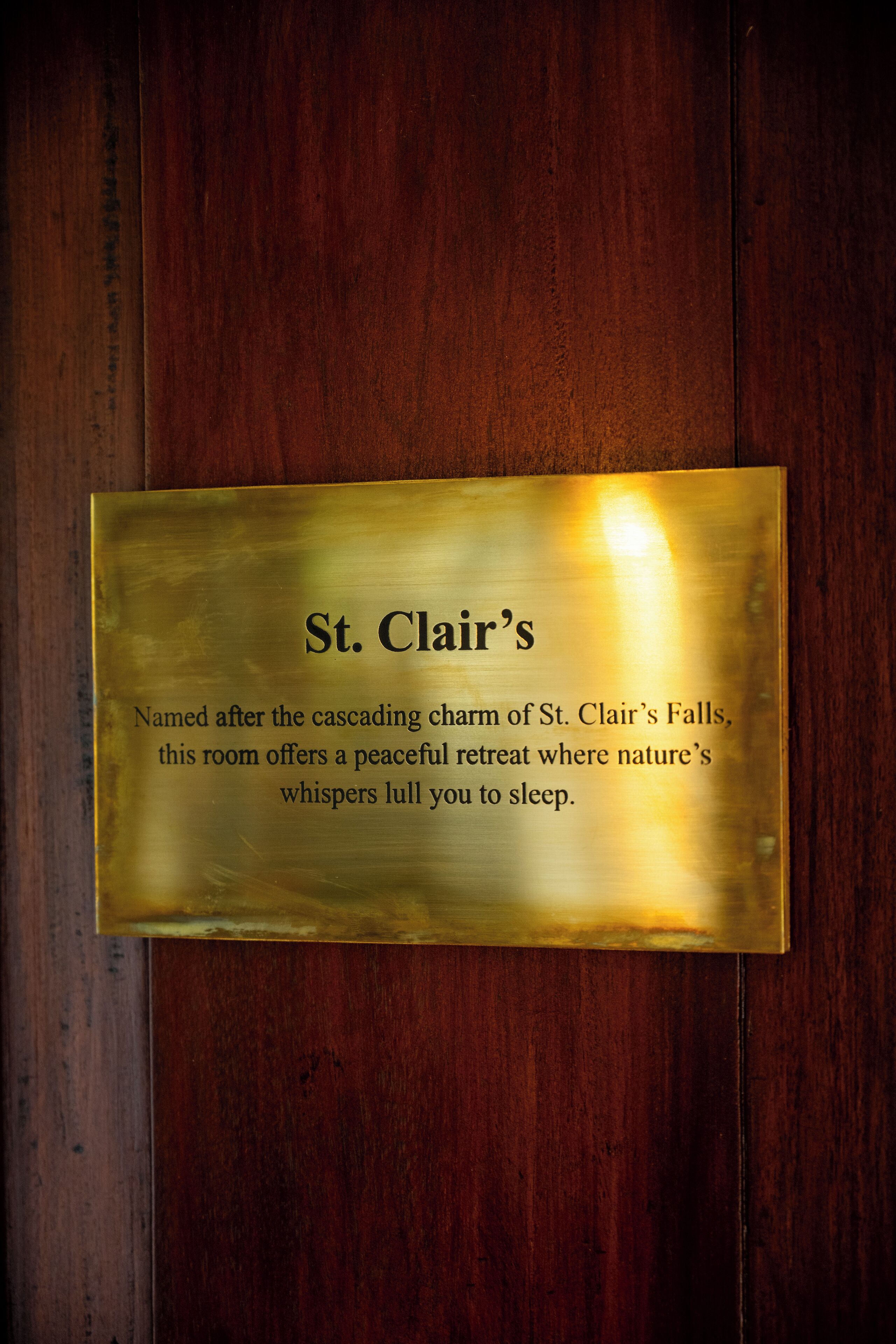 Una placa en una pared de madera con texto que describe una habitación nombrada en honor a las Cataratas St. Clair, que ofrece un refugio tranquilo.