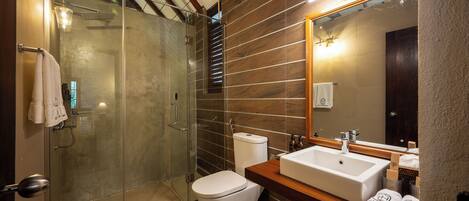 A modern bathroom with a glass shower enclosure, a white toilet, and a wooden vanity with a large mirror.