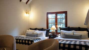 Habitación de hotel con dos camas, una silla, una lámpara y ventana con vistas a árboles.