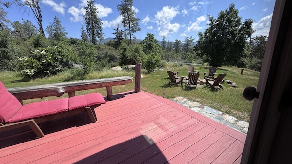 A deck with a red floor, a wooden bench, and two Adirondack chairs.