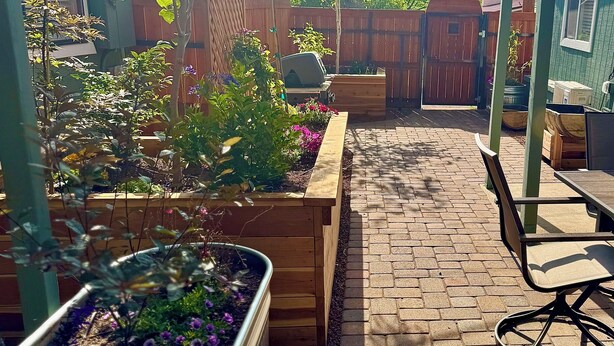 A backyard with raised garden beds, a brick patio, and a wooden fence. - Outlaw Hideaway Downtown (Prescott)