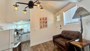 A modern kitchen with white cabinets, a wooden countertop, and a built-in oven. There is a brown leather sofa and a wooden table with a lamp. The floor is wooden, and there is a window with blinds. - Outlaw Hideaway Downtown (Prescott)
