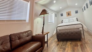 A bedroom with a bed, a brown leather sofa, a lamp, and wooden flooring. - Outlaw Hideaway Downtown (Prescott)