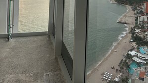 A balcony with a view of a beach and ocean, large windows, and a clear sky. - Beachfront Studio with Balcony, Rooftop Pool & Gym Access (Puerto Vallarta)