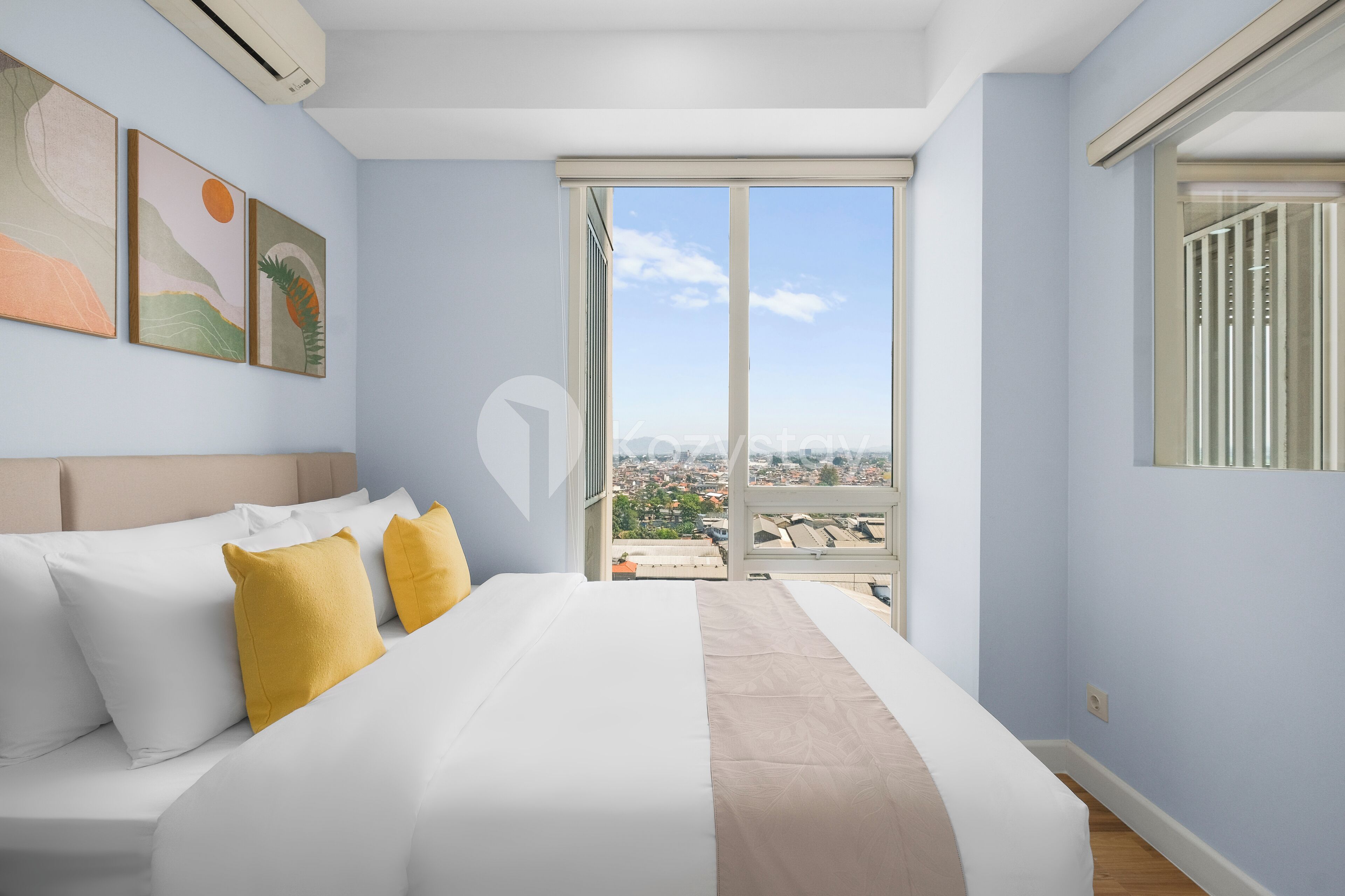 A modern hotel room with a large bed, a city view through a sliding door, and artwork on the wall.