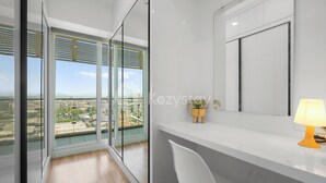 Una habitación de hotel moderna con ventanas amplias, un escritorio blanco y vistas a la ciudad.