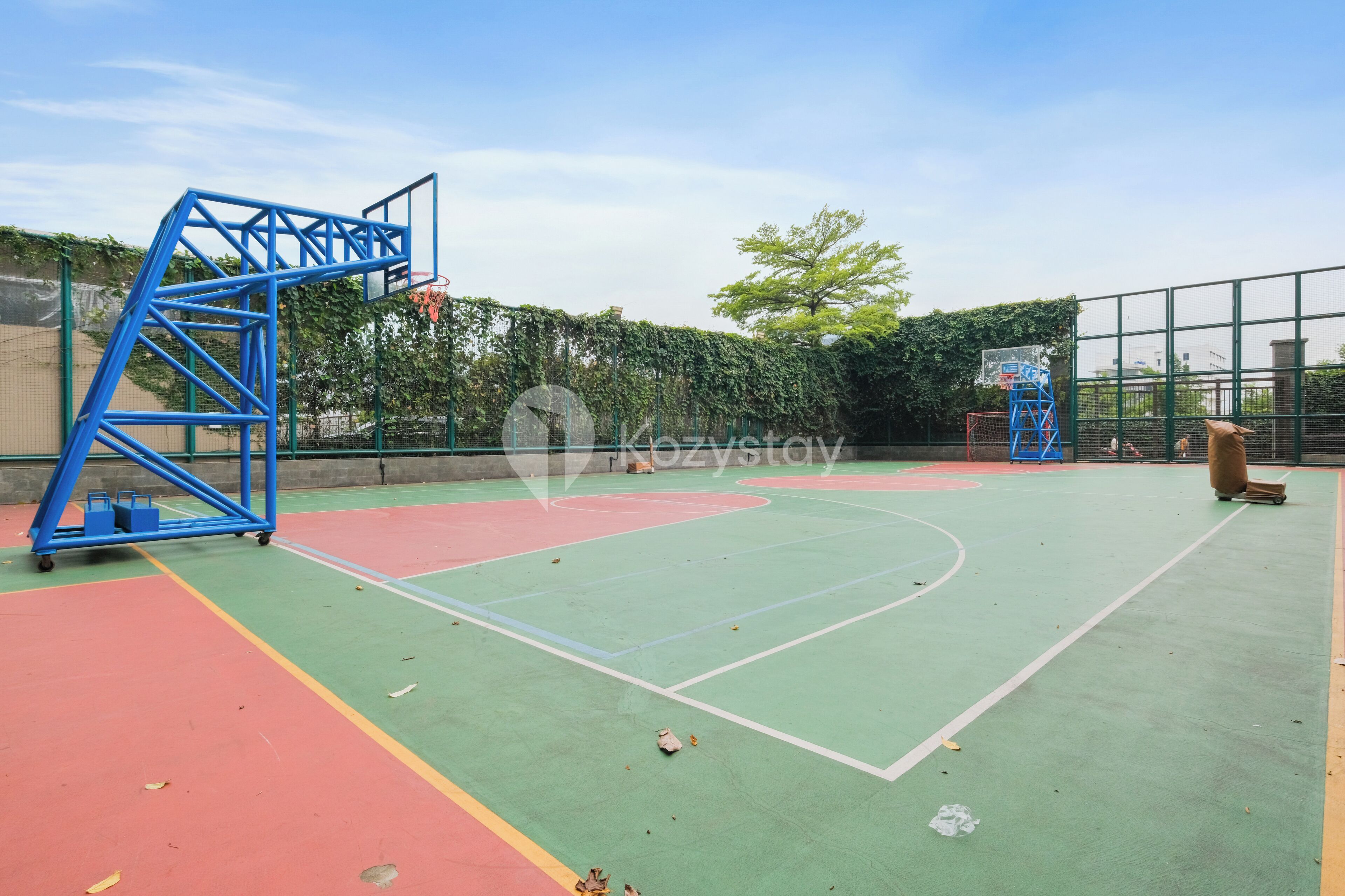 Een buitenbasketbalveld met een blauwe metalen constructie, een basketbalring en een net.