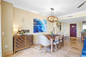 A dining area with a wooden table, wicker chairs, a chandelier, and a large abstract painting on the wall. - 2 Honua Kai Villas | Ocean View | Sleeps 14 | Free Car w/ 6+ Nights | ML-1285 (Lahaina)