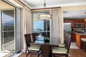 Een eetruimte met een glazen tafel, stoelen, uitzicht op de oceaan en een keuken met moderne apparatuur.
