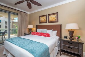 Une chambre d’hôtel comprenant un lit, deux lampes de chevet, une table de chevet, un ventilateur de plafond et une porte-fenêtre coulissante donnant sur un balcon.