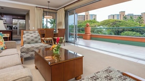 Una sala moderna con sofá, sillón y mesa de centro, una zona de cocina y un balcón con vistas a edificios y zonas verdes.