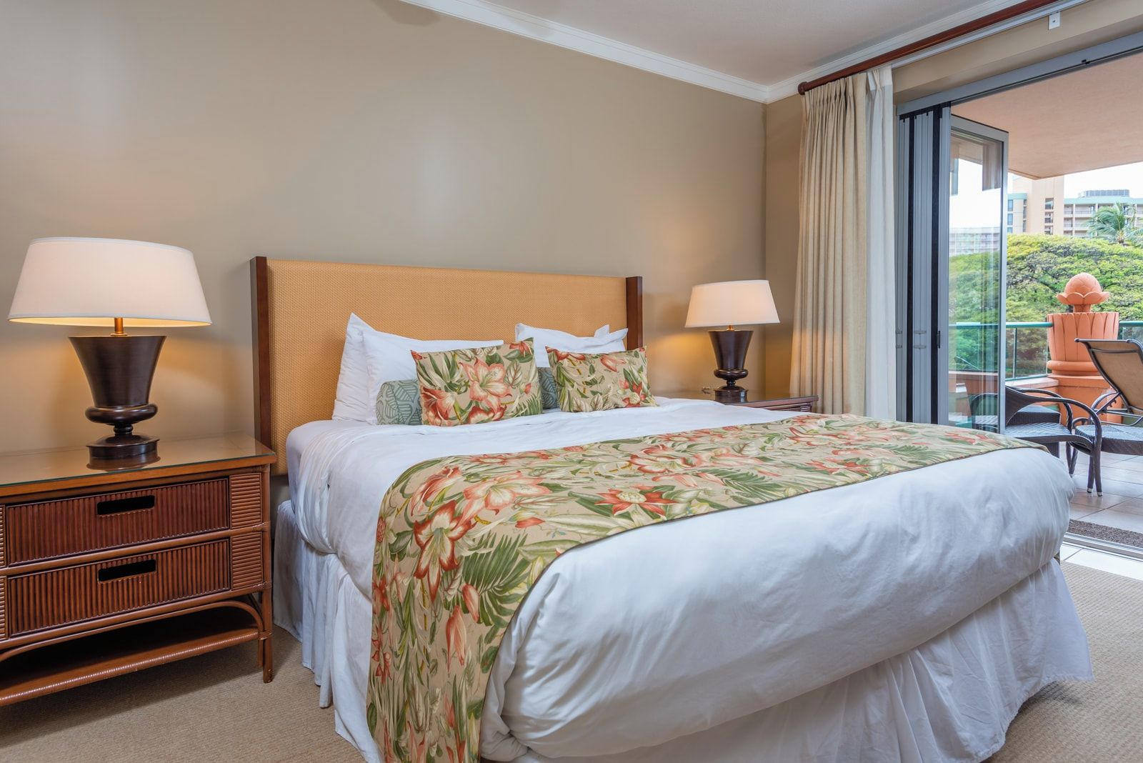 Una habitación de hotel con una cama, dos mesitas de noche con lámparas, una mesita auxiliar y un balcón con una silla.