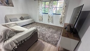 A bedroom with a bed, a desk, a TV, and a window with curtains.