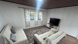 A room with a sofa, a bed, a TV, and a window with curtains.