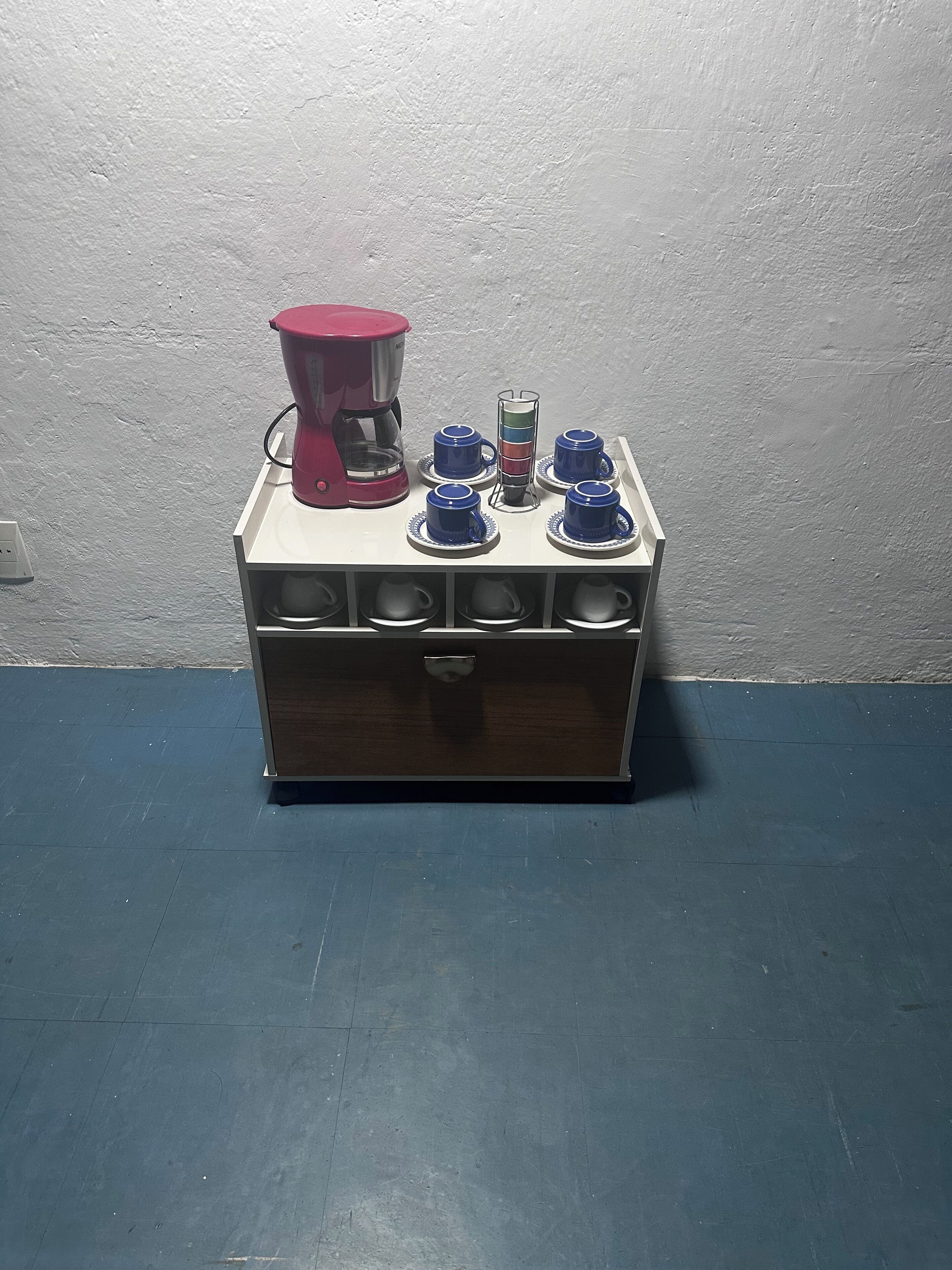 A coffee maker on a white countertop with six blue mugs and a coffee pot.