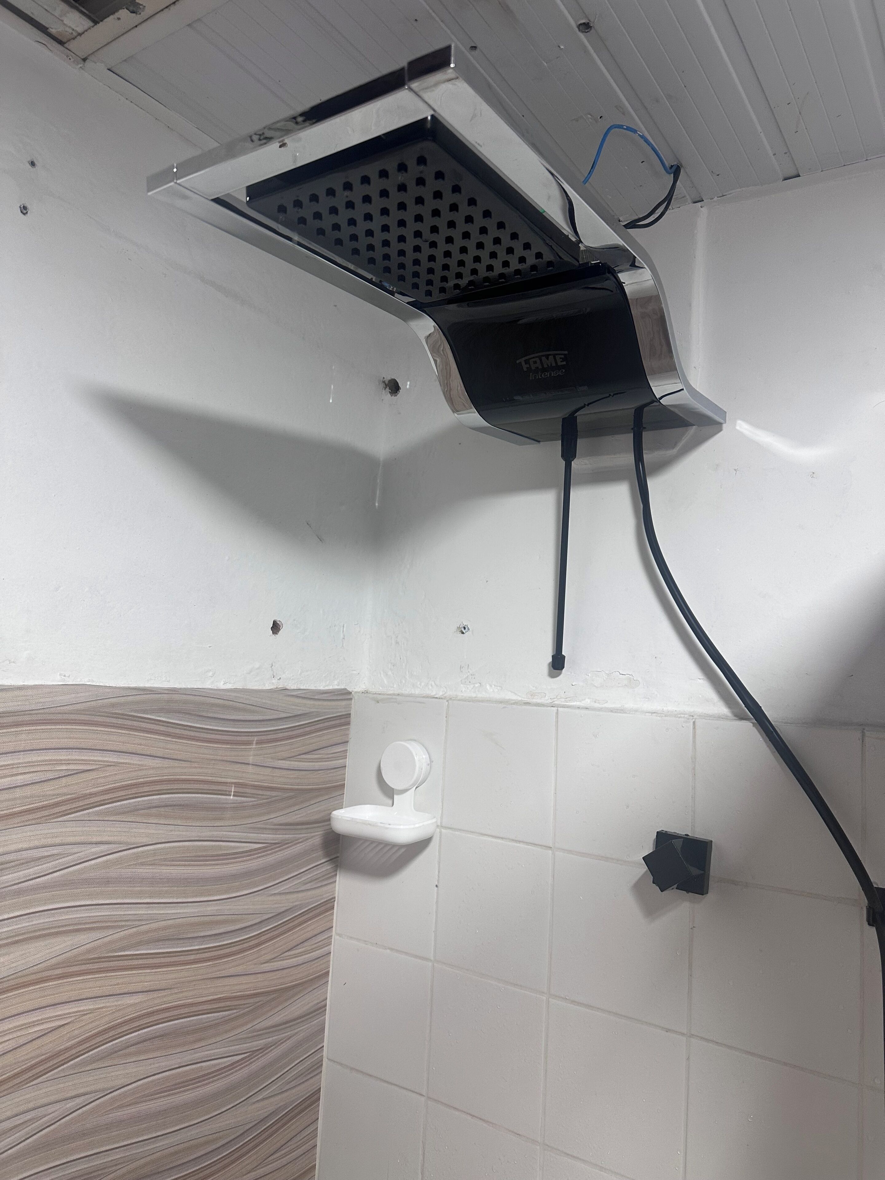 A corner of a bathroom with a shower head, a white toilet, and a tiled wall.