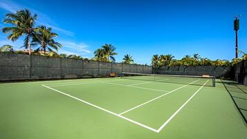 A tennis court with a net, surrounded by a black wall and palm trees.