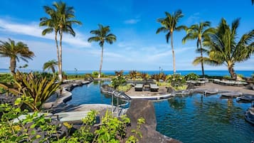 A pool area with palm trees, lounge chairs, and a view of the ocean.