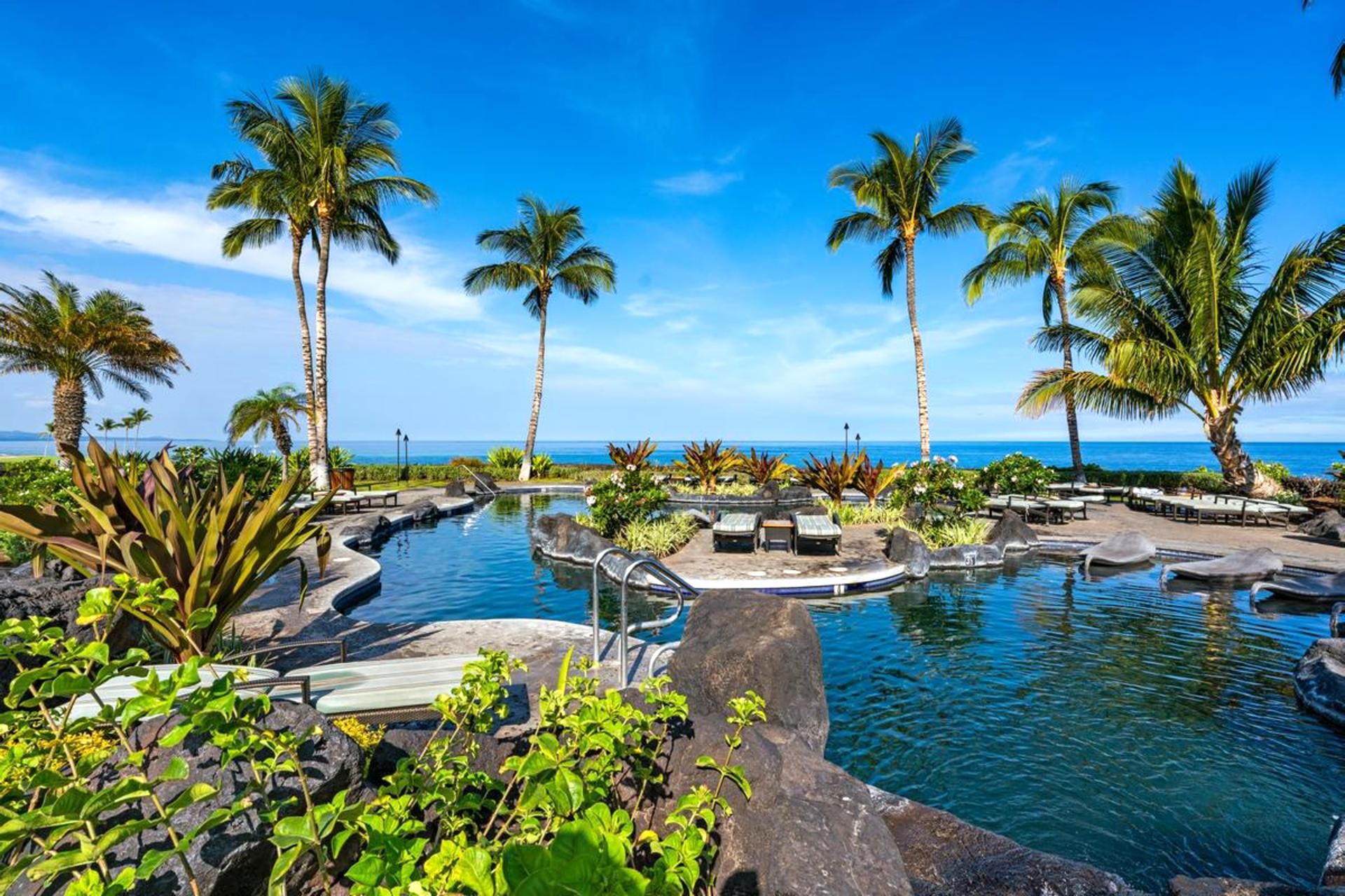 A pool area with palm trees and a view of the ocean.