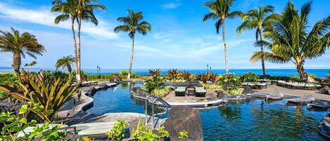 A pool area with palm trees and a view of the ocean.