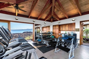 Un gimnasio con cintas de correr, máquinas de pesas y pelotas de ejercicio, con vistas a un paisaje pintoresco.