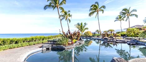 A clear pool with a view of the ocean, surrounded by palm trees and rocks.