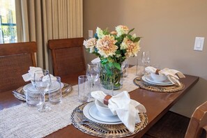 Una mesa de comedor dispuesta con cristalería transparente, platos y un centro de mesa con flores.