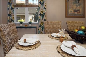 Un comedor con una mesa dispuesta para cuatro personas, sillas de mimbre, un jarrón con flores secas y una cesta con huevos de colores.