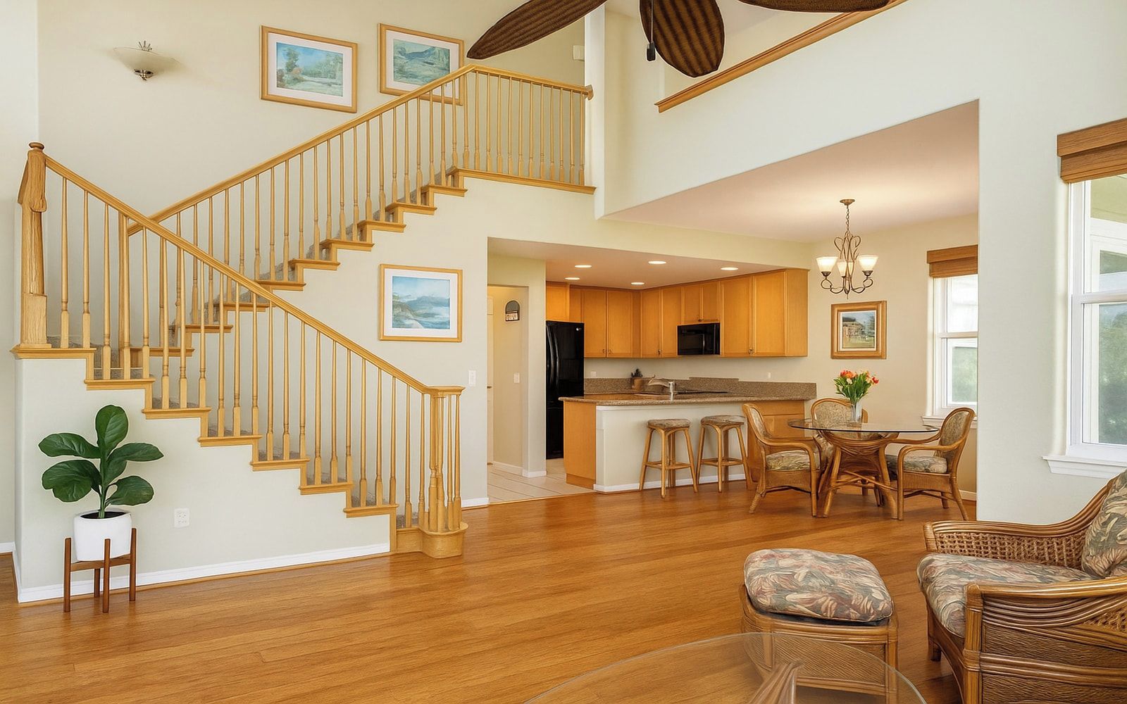A spacious living area with a wooden staircase, a kitchen with a central island, and a dining area with wicker furniture.