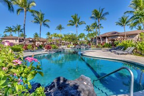 A swimming pool surrounded by palm trees and lounge chairs, with a clear blue sky above.