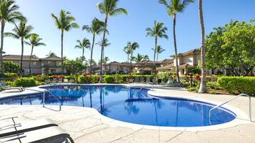 A swimming pool with lounge chairs, surrounded by palm trees and a residential building.