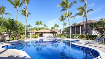 A swimming pool surrounded by palm trees and lounge chairs, with a building in the background.