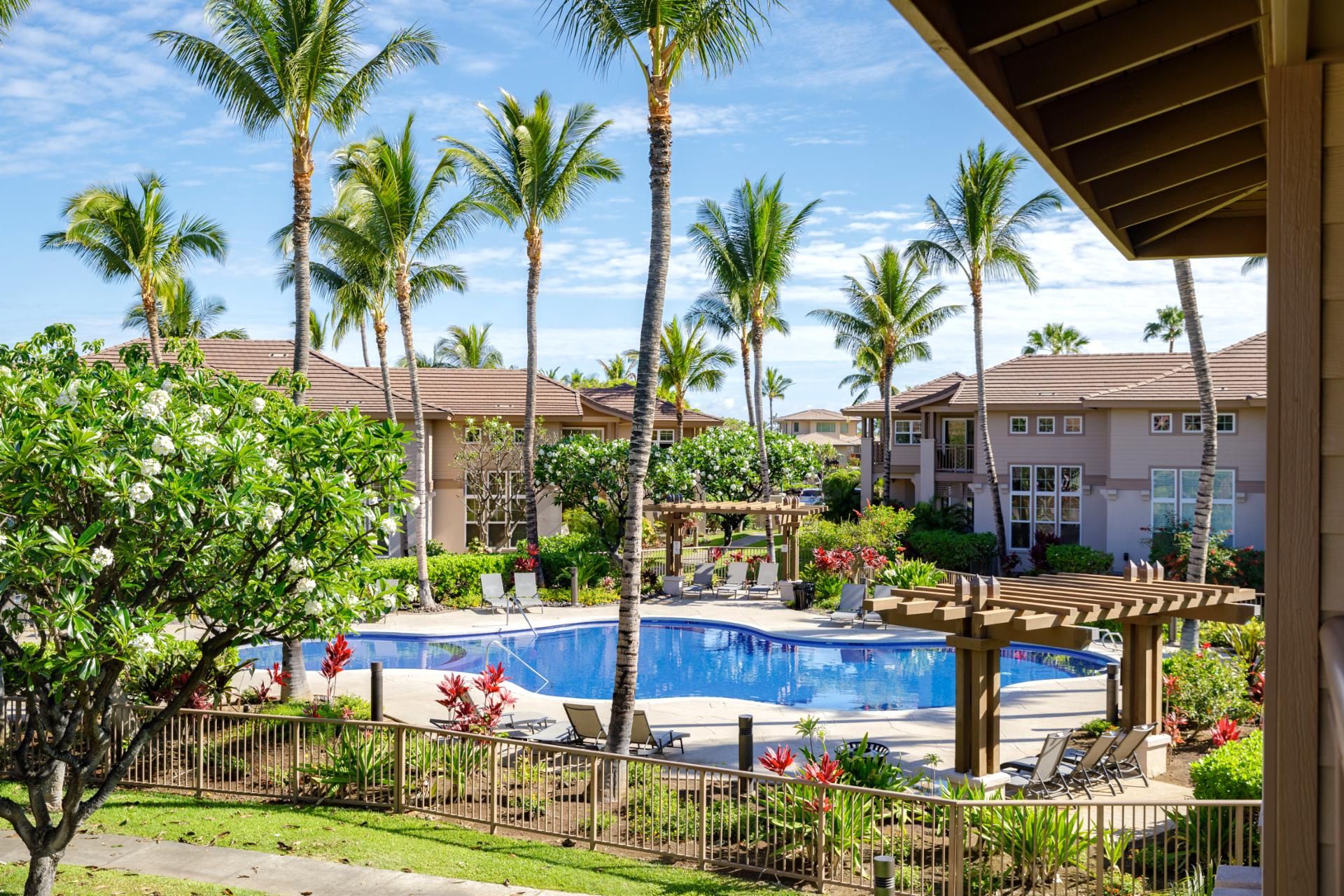 A pool area with lounge chairs, palm trees, and a building with a tiled roof.