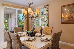 Un coin repas avec une table dressée pour six personnes, entouré de chaises en osier, d’un lustre et offrant une vue sur la verdure à l’extérieur.