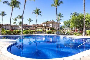 A swimming pool surrounded by palm trees and a building with a tiled roof.