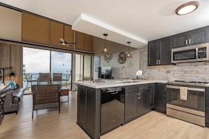 Una cocina moderna con una isla grande, armarios oscuros, electrodomésticos de acero inoxidable y vistas al exterior.
