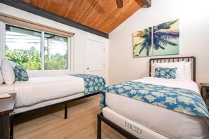 A bedroom with two beds, a window with a view of greenery, and a painting of palm trees.