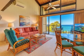 A spacious living area with a sofa, chairs, a coffee table, and a balcony with a view of the ocean.