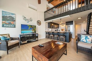 A spacious living area with a large TV, a wooden coffee table, and a kitchen with bar stools. - Napili Point | Oceanfront 5 BR, Sleeps 14 | Car Incl. w/ 6+ Nights | NAP ML-1301 by KBM (Lahaina)