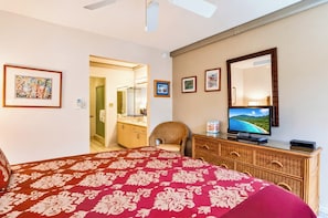 A hotel room with a bed, a television, a wicker chair, a dresser, and a bathroom visible through an open door. - Napili Point | Oceanfront 5 BR, Sleeps 14 | Car Incl. w/ 6+ Nights | NAP ML-1301 by KBM (Lahaina)