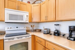 A kitchen with wooden cabinets, a white microwave, a stove, a toaster, a blender, and a coffee maker.