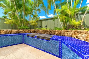 A swimming pool with blue mosaic tiles, surrounded by a stone wall and tropical plants.