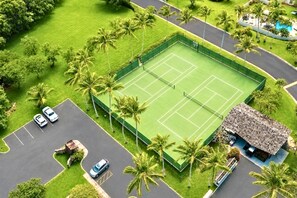 An aerial view of a tennis court surrounded by palm trees and a parking lot with cars. - Kuilima Estates | Oceanfront 3 BR, Sleeps 10 | Car Incl. w/ 6+ Nights | KUL ML-1303 by KBM (Kahuku)