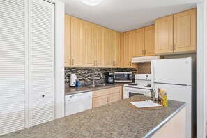 A kitchen with wooden cabinets, a granite countertop, a microwave, a coffee maker, and a refrigerator.