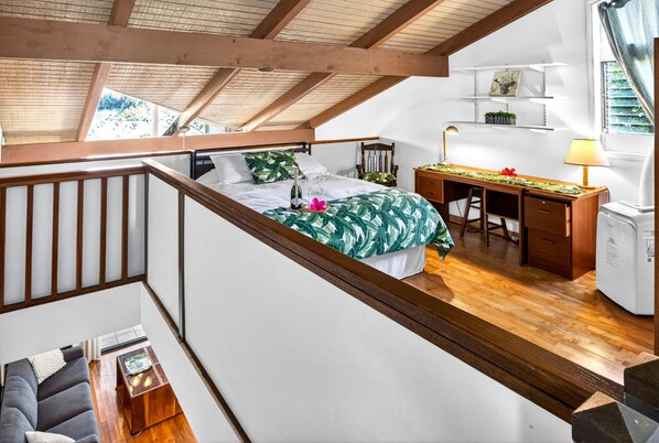 A bedroom with a bed, a desk, and a chair. There is a staircase leading to another room.