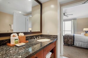 A hotel bathroom with a granite countertop, sink, mirror, and toiletries.