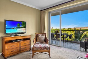 A room with a TV, wooden furniture, a wicker chair, and a balcony with a view. - Honua Kai | Ocean View 4 BR, Sleeps 14 | Car Incl. w/ 6+ Nights | HKK ML-1305 by KBM (Lahaina)